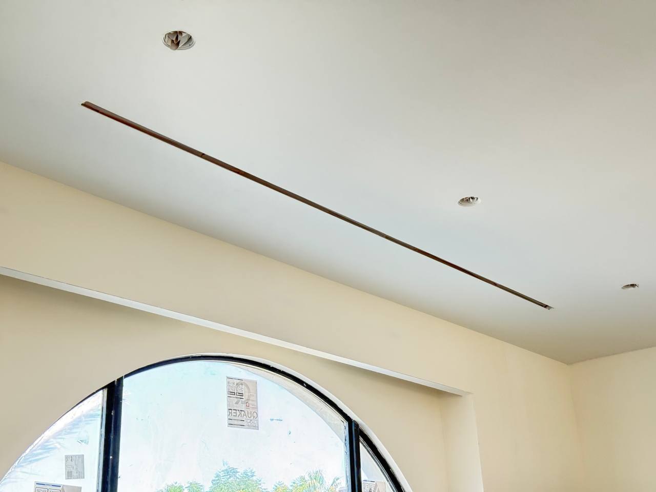 Long linear slot grille integrated into a smooth ceiling above an arched window