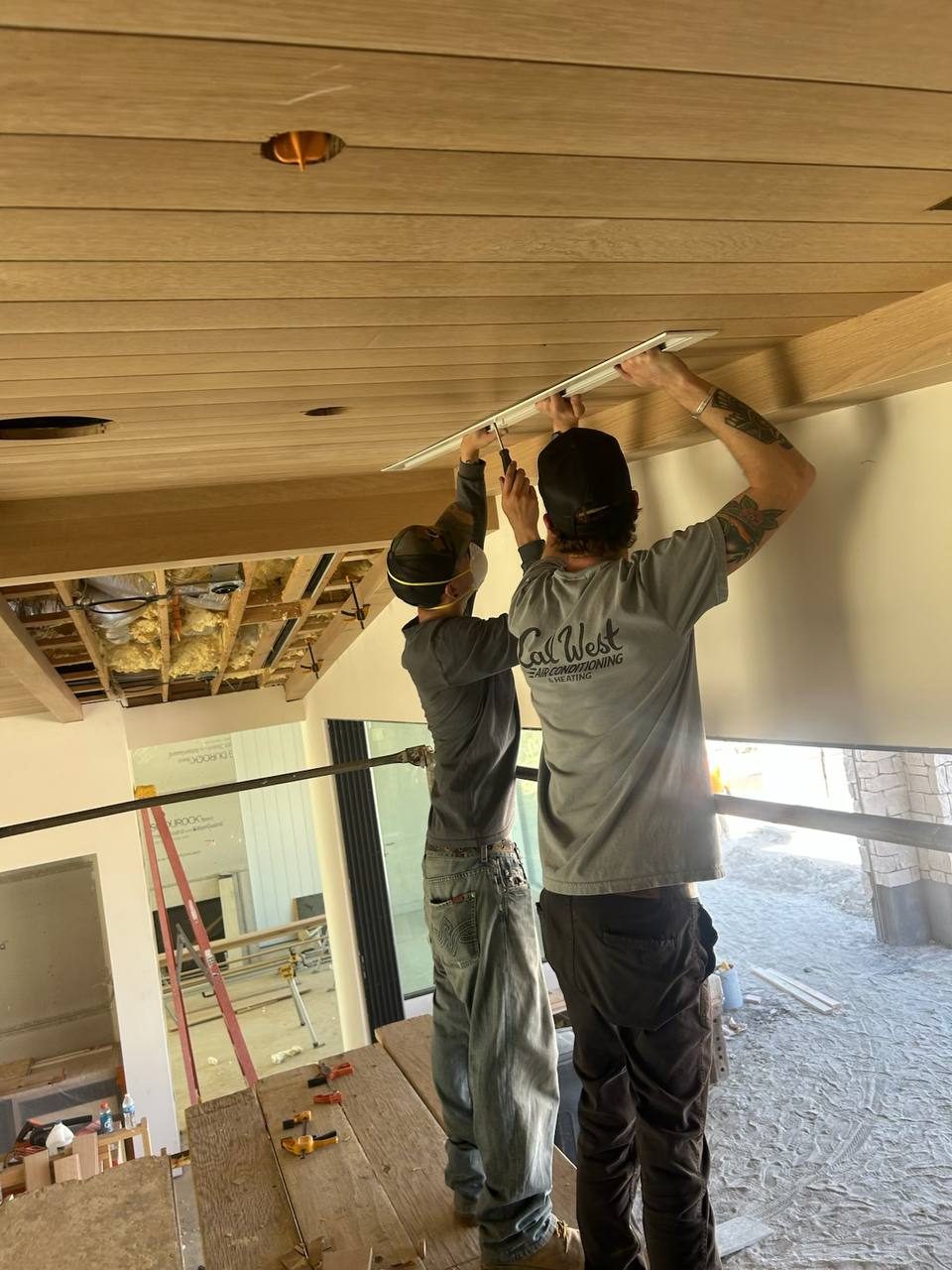 Ethan Barnard and Nathan Lopez fitting the final finish trim on a linear register in a tongue-and-groove great room ceiling